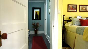 A hallway with a red rug leading to a bedroom with a bed, a nightstand, and a wall with two framed pictures.