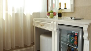 Un mini bar blancet amb un bol de vidre ple de pomes, dues ampolles de xampany i una llauna de Sprite.