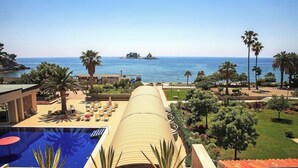 A resort with a pool, lounge chairs, palm trees, and a view of the ocean. - Palas (Petrovac)