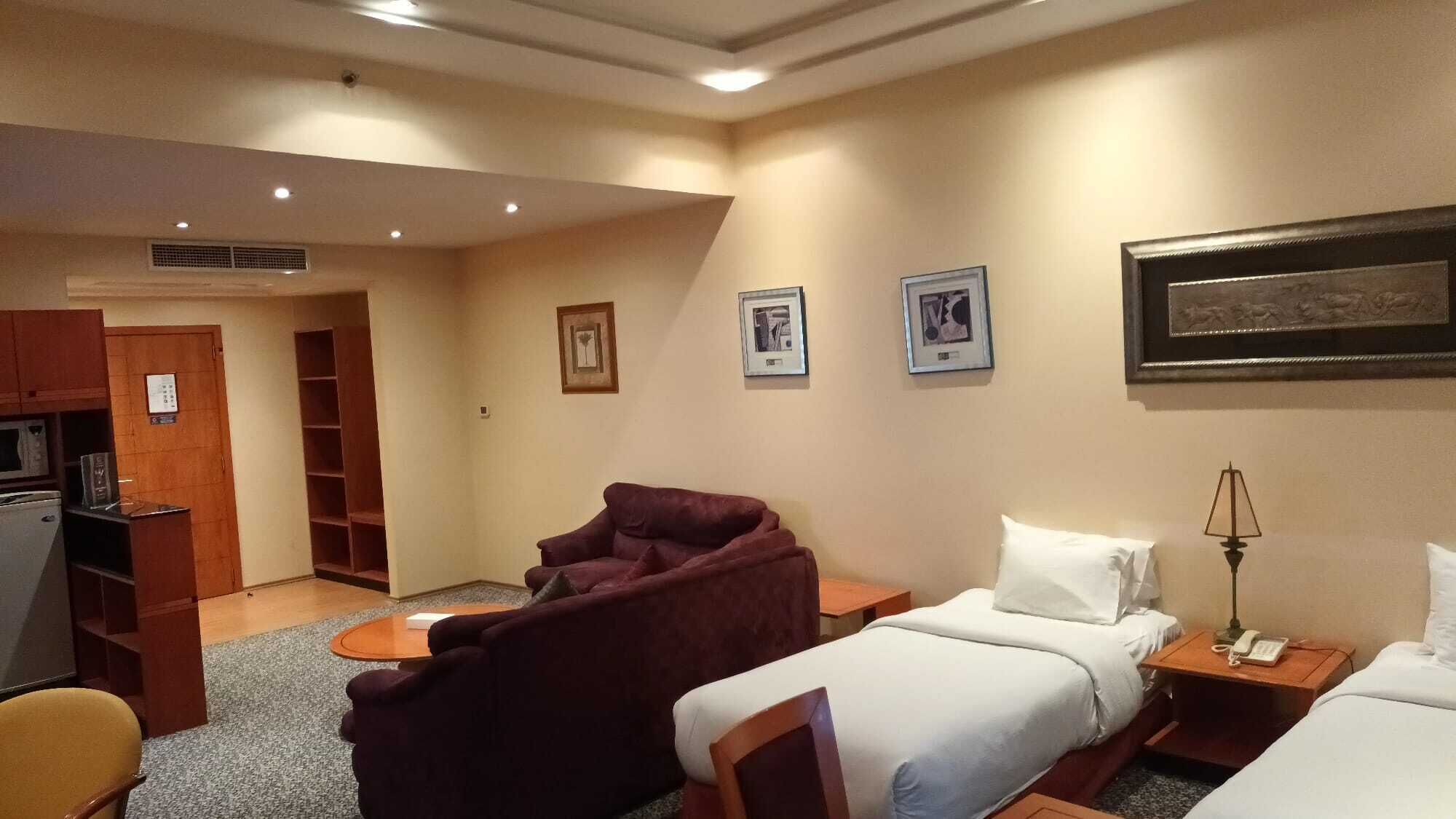 Quarto de hotel com cama, cadeira, escrivaninha, abajur e televisão.