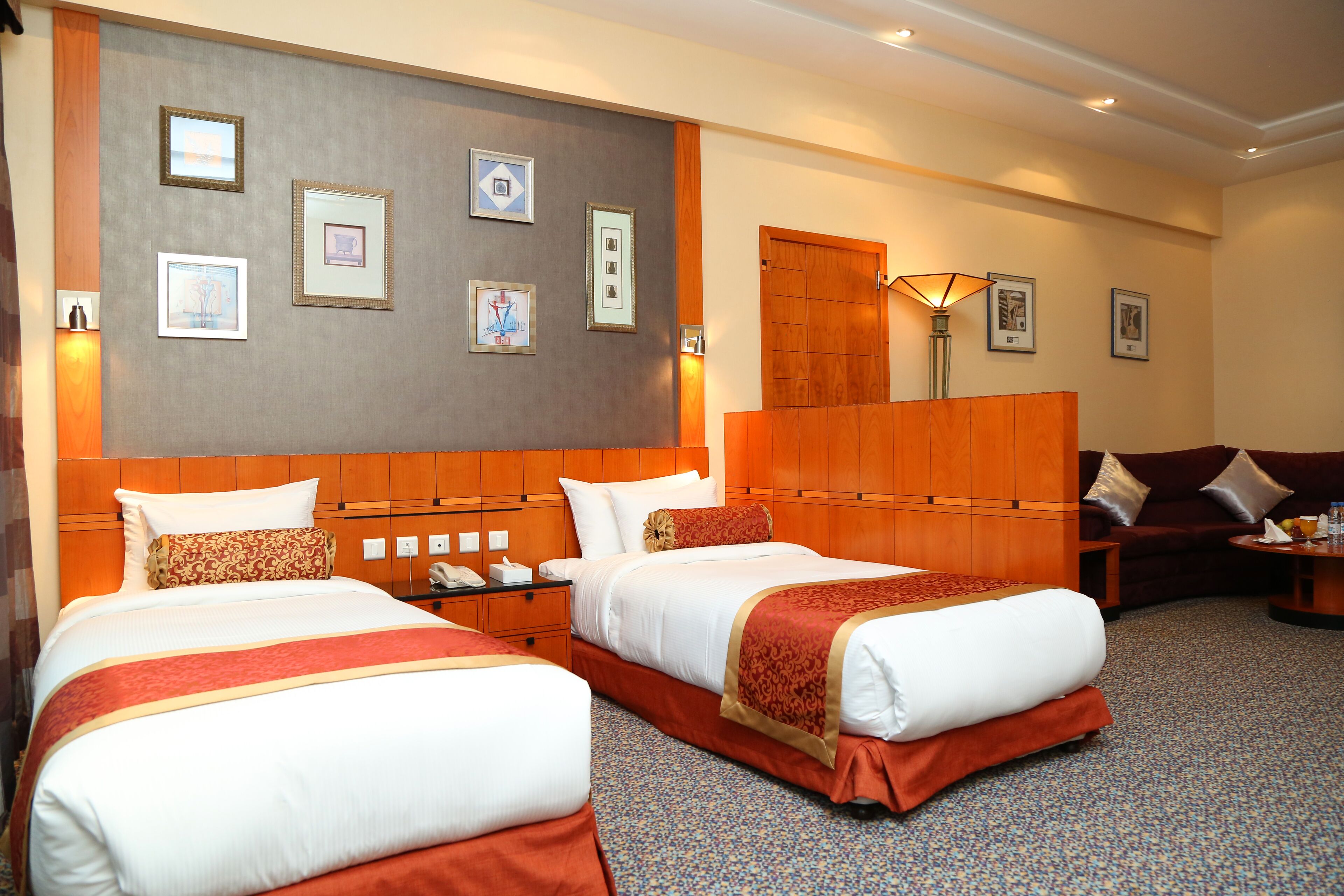 Habitación de hotel con dos camas, cabecero de madera, sofá y cuadros en la pared.