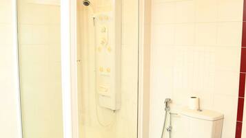 A bathroom with a glass-enclosed shower, a toilet, and a trash can.