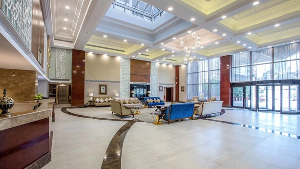 A spacious lobby with a reception desk, seating area, and large windows offering views of the city. - Gulf Court Hotel (Manama)