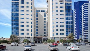 The Gulf Court Hotel with a modern facade, multiple floors, and a parking lot with several cars. - Gulf Court Hotel (Manama)