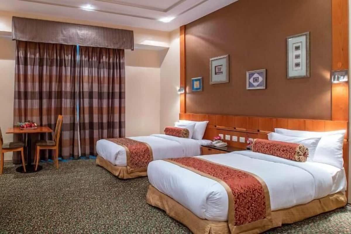 Una camera d'albergo con due letti, una scrivania, una sedia, una lampada e una ciotola di frutta.