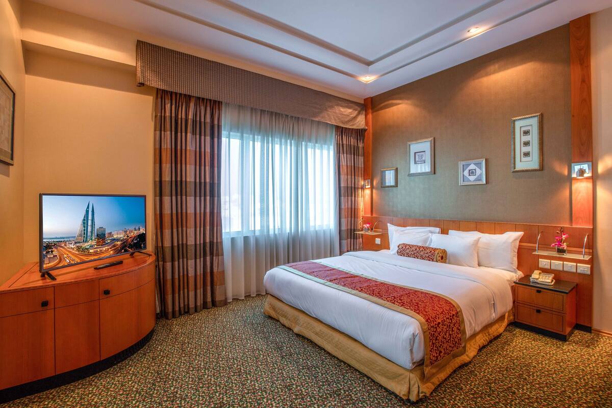 Camera d'albergo con un letto grande, una TV su un mobile in legno, un comodino con una lampada e vista sulla città.