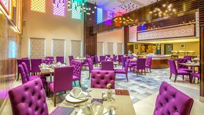 A spacious dining area with purple upholstered chairs and tables, a central bar area, and patterned floor tiles. - Gulf Court Hotel (Manama)