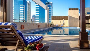 A poolside area with lounge chairs, a pool, and modern buildings in the background. - Gulf Court Hotel (Manama)