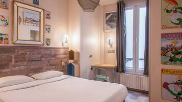 A hotel room with a bed, a wooden headboard, a window with curtains, and wall decorations including framed pictures and posters.