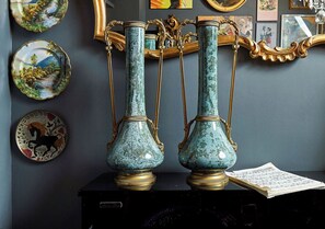 Two ornate vases with gold accents on a dark surface, surrounded by framed artwork on a wall.