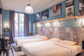 A hotel room with two beds, a desk, a chair, a window with curtains, and patterned wall tiles.