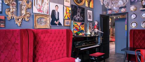 A room with a red upholstered sofa, a black piano, and a marble coffee table.