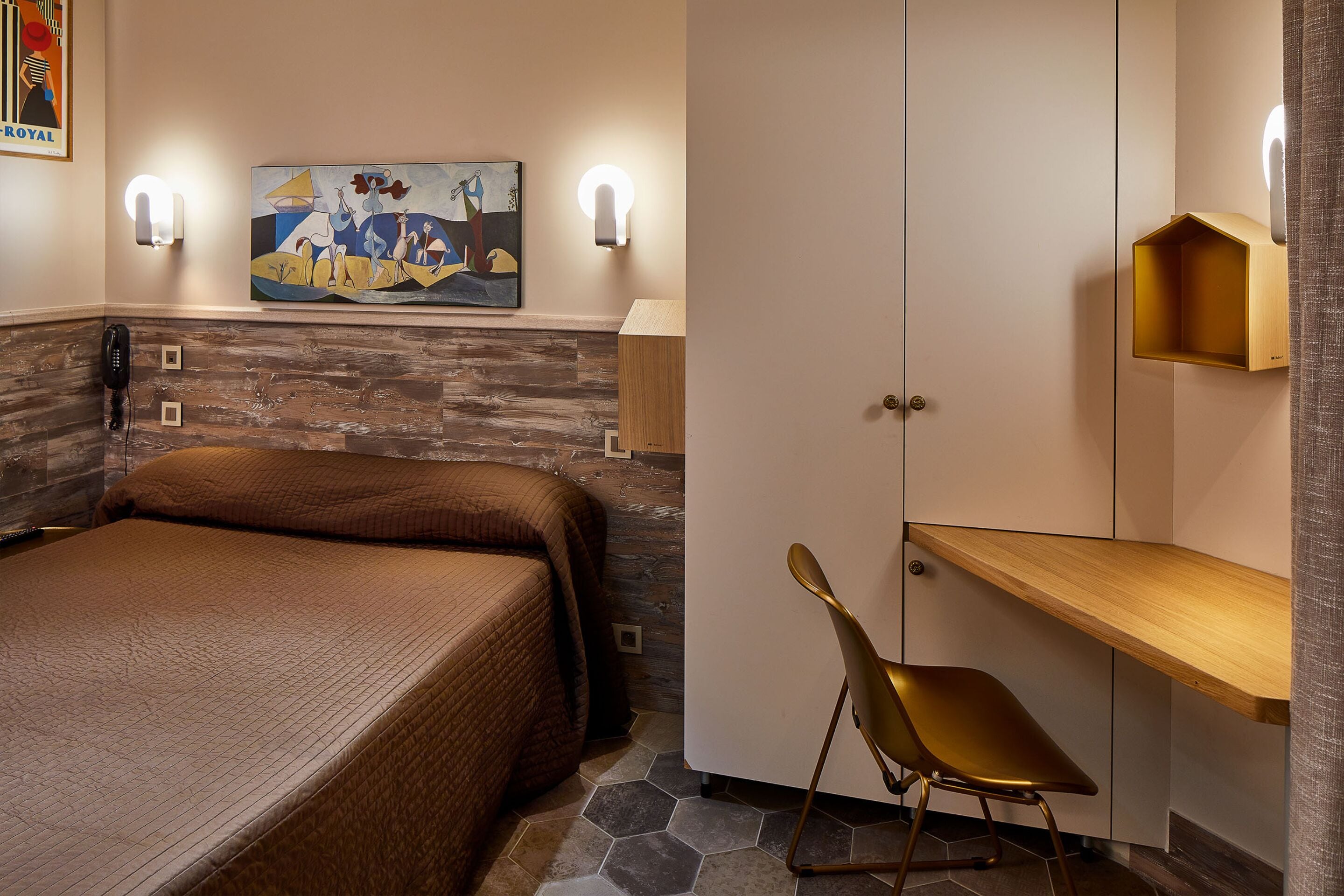 Habitación de hotel con cama, escritorio y silla. Hay un cuadro en la pared y un teléfono en la mesita de noche.