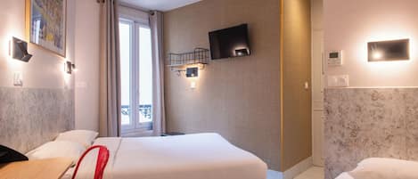 Habitación de hotel con cama, escritorio, silla, televisión y ventana con cortinas.