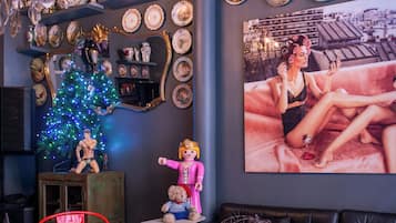 A room with a chandelier, a Christmas tree, a red chair, a black sofa, a marble table, and a large framed picture on the wall.