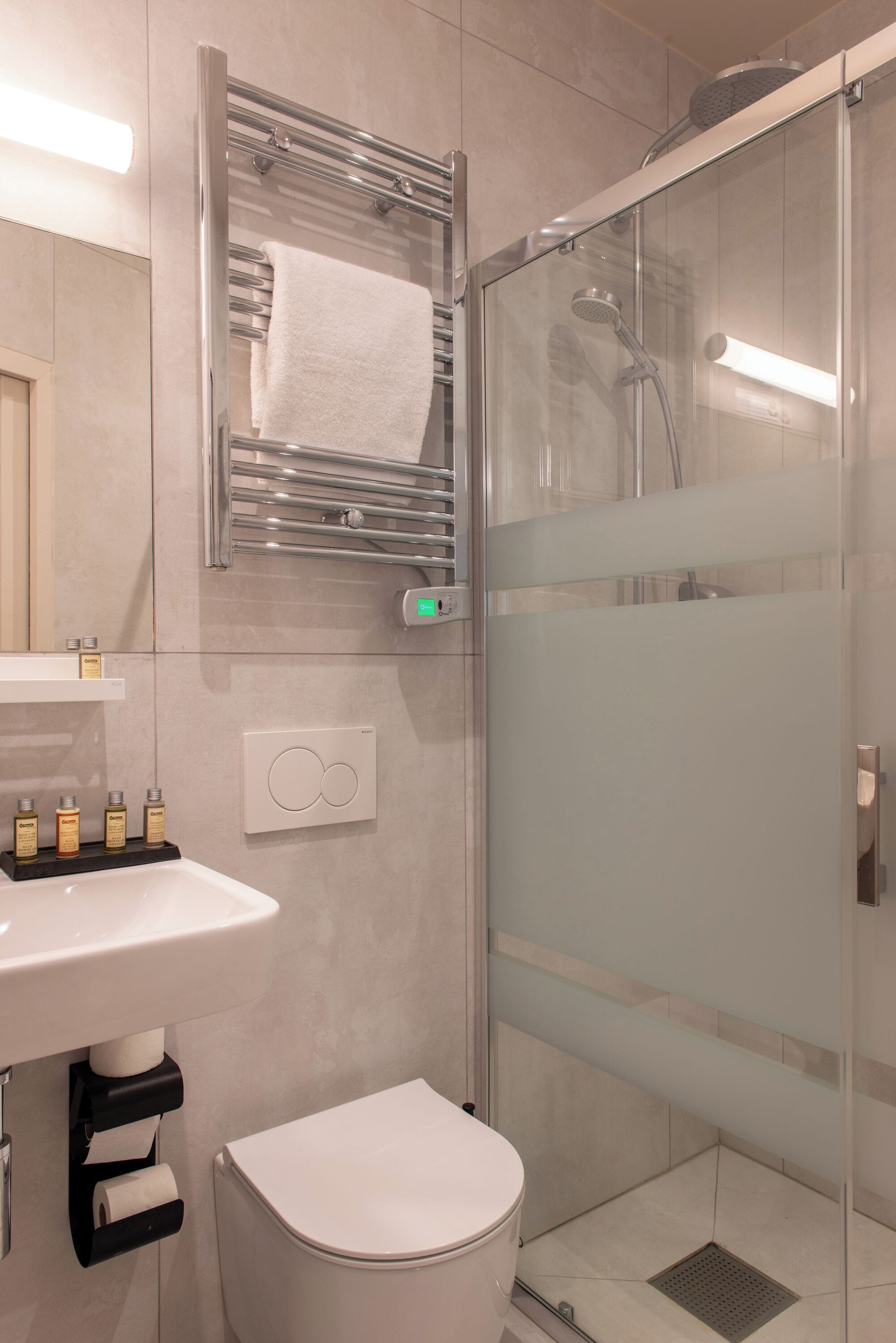 A modern bathroom with a glass-enclosed shower, a white toilet, and a sink with a towel rack above it.