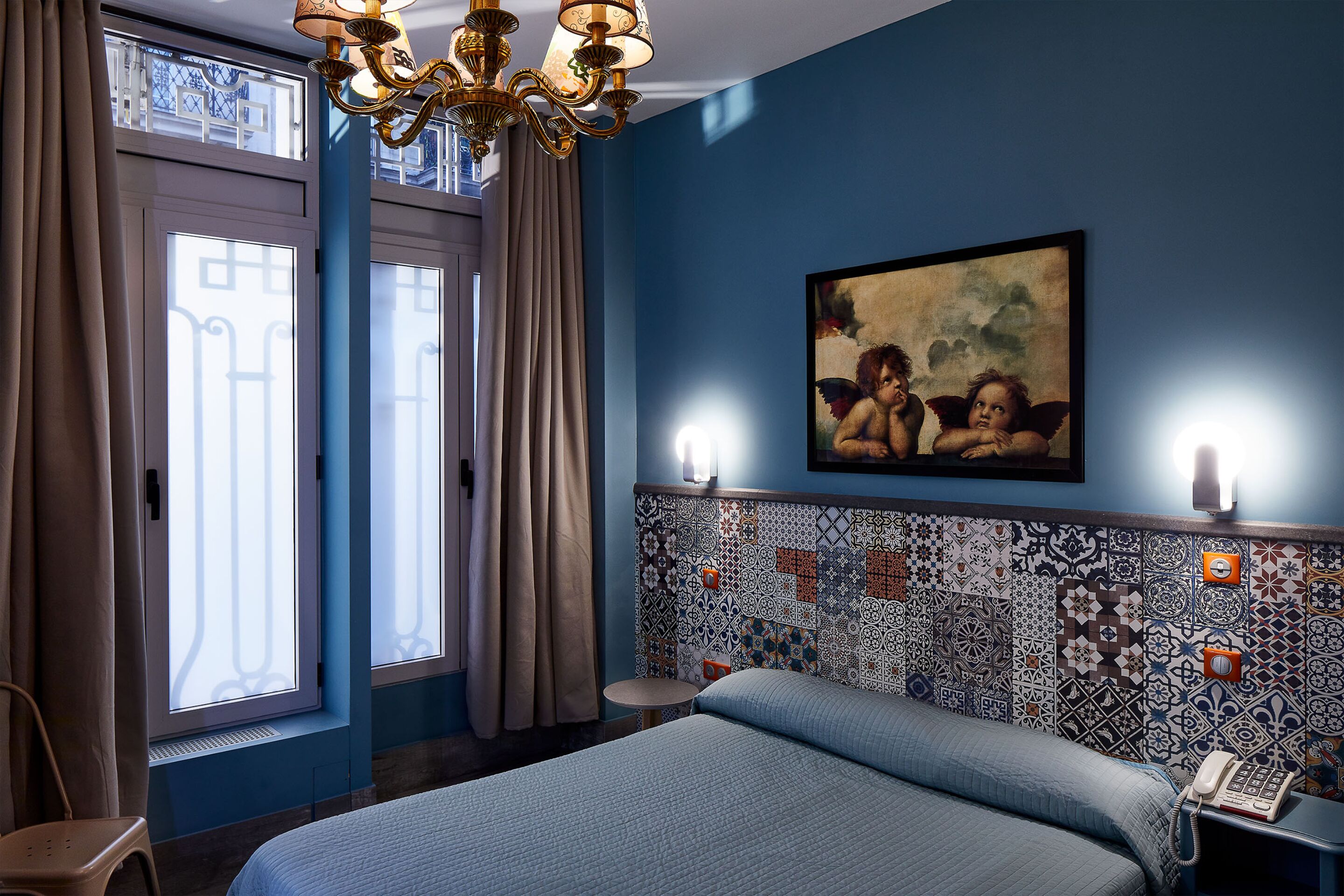 A bedroom with a bed, a chandelier, a painting, and a patterned wall.