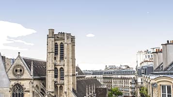 Une église historique dotée d’un haut clocher, une rue bordée de voitures garées et un ciel dégagé.