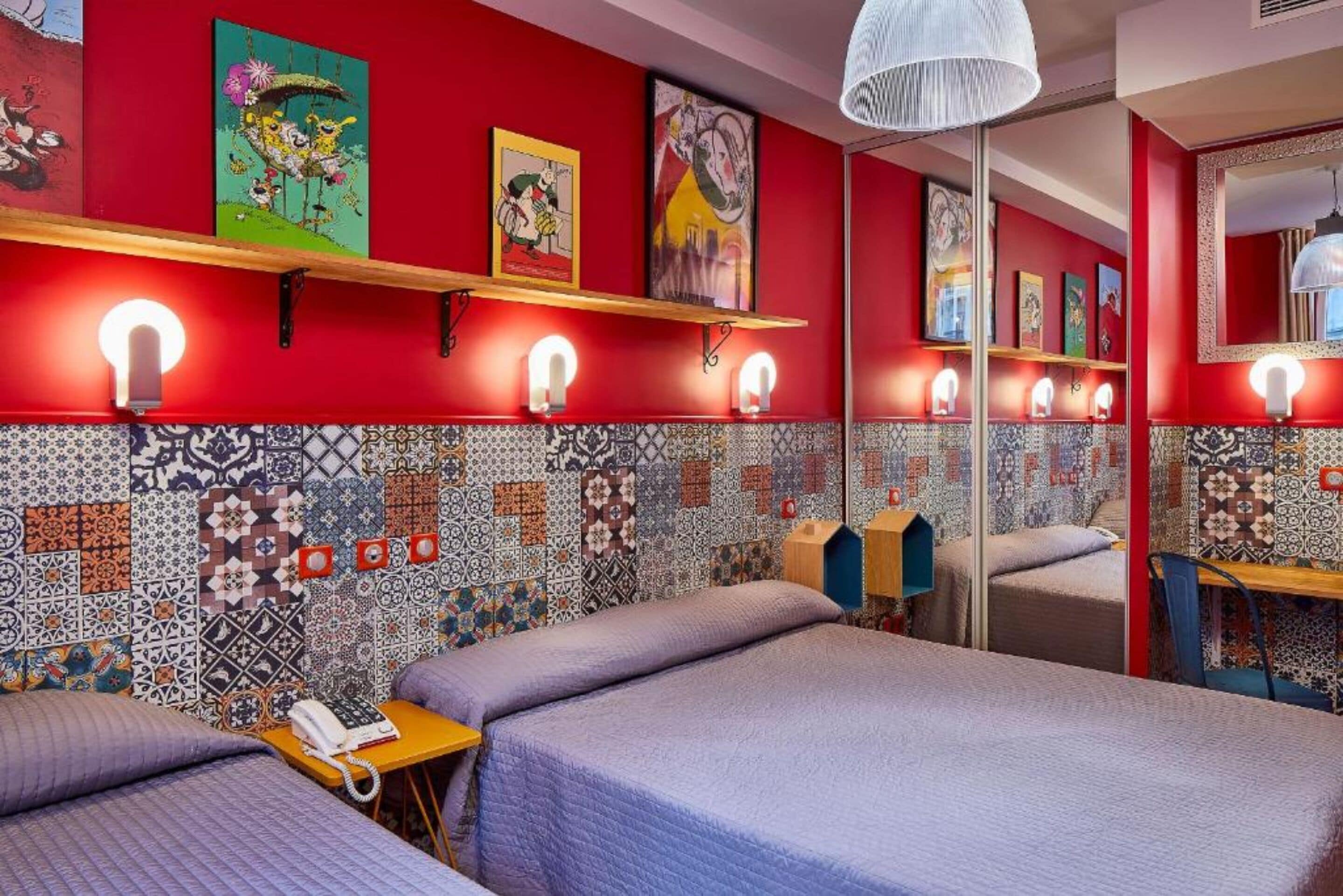 Habitación de hotel con dos camas, una pared roja con azulejos estampados y obras de arte sobre las camas.