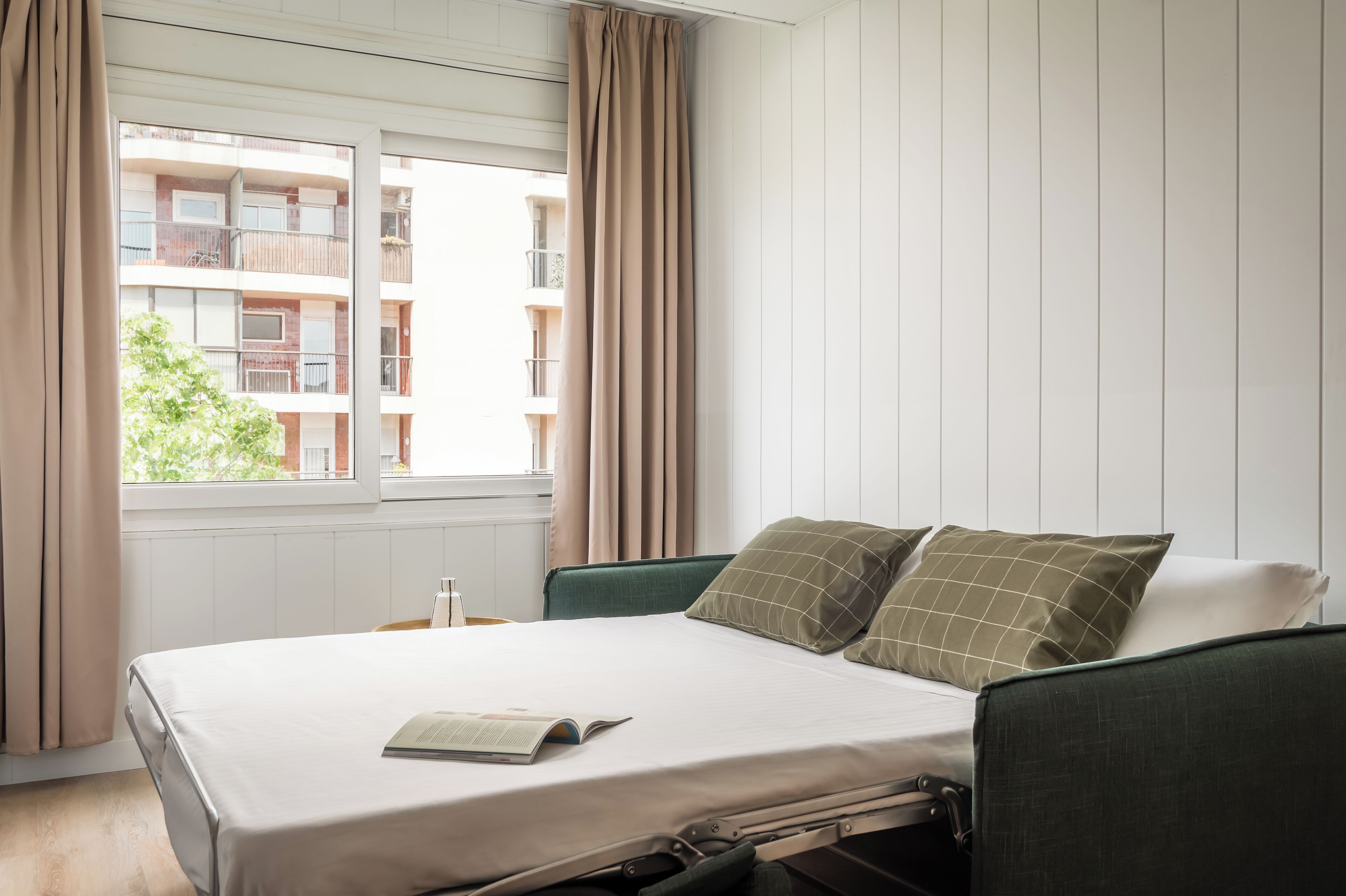 Habitación de hotel con cama, ventana con cortinas y vista a un edificio.