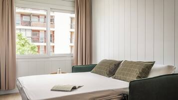 Habitación de hotel con cama, ventana con cortinas y vista a un edificio.
