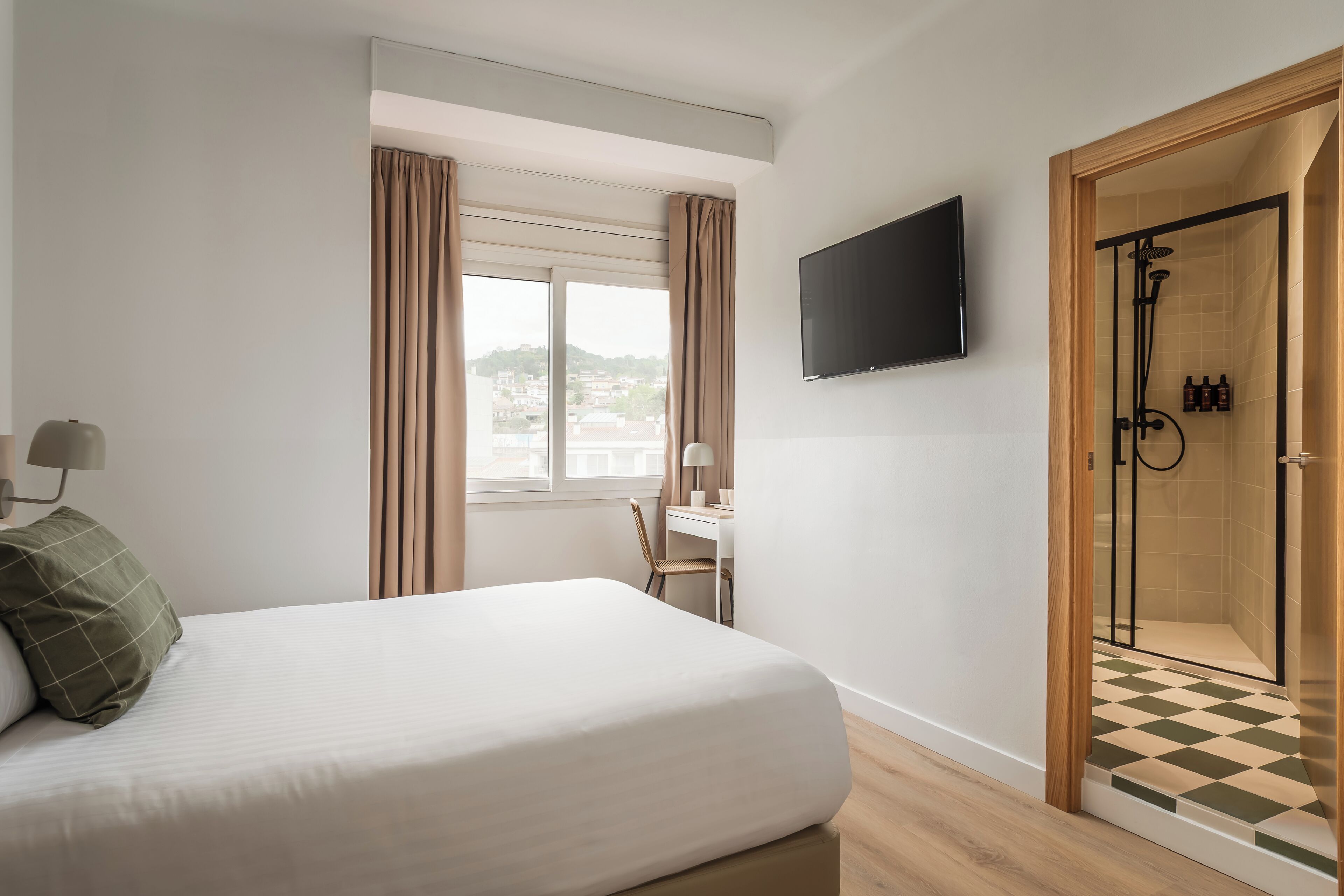 Una habitación de hotel con cama, escritorio, televisión y zona de ducha.