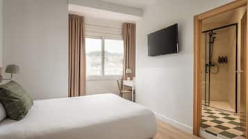 Una habitación de hotel con cama, escritorio, televisión y zona de ducha.