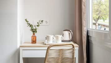 A corner desk with a woven chair, a vase with green leaves, two white mugs, and a kettle.