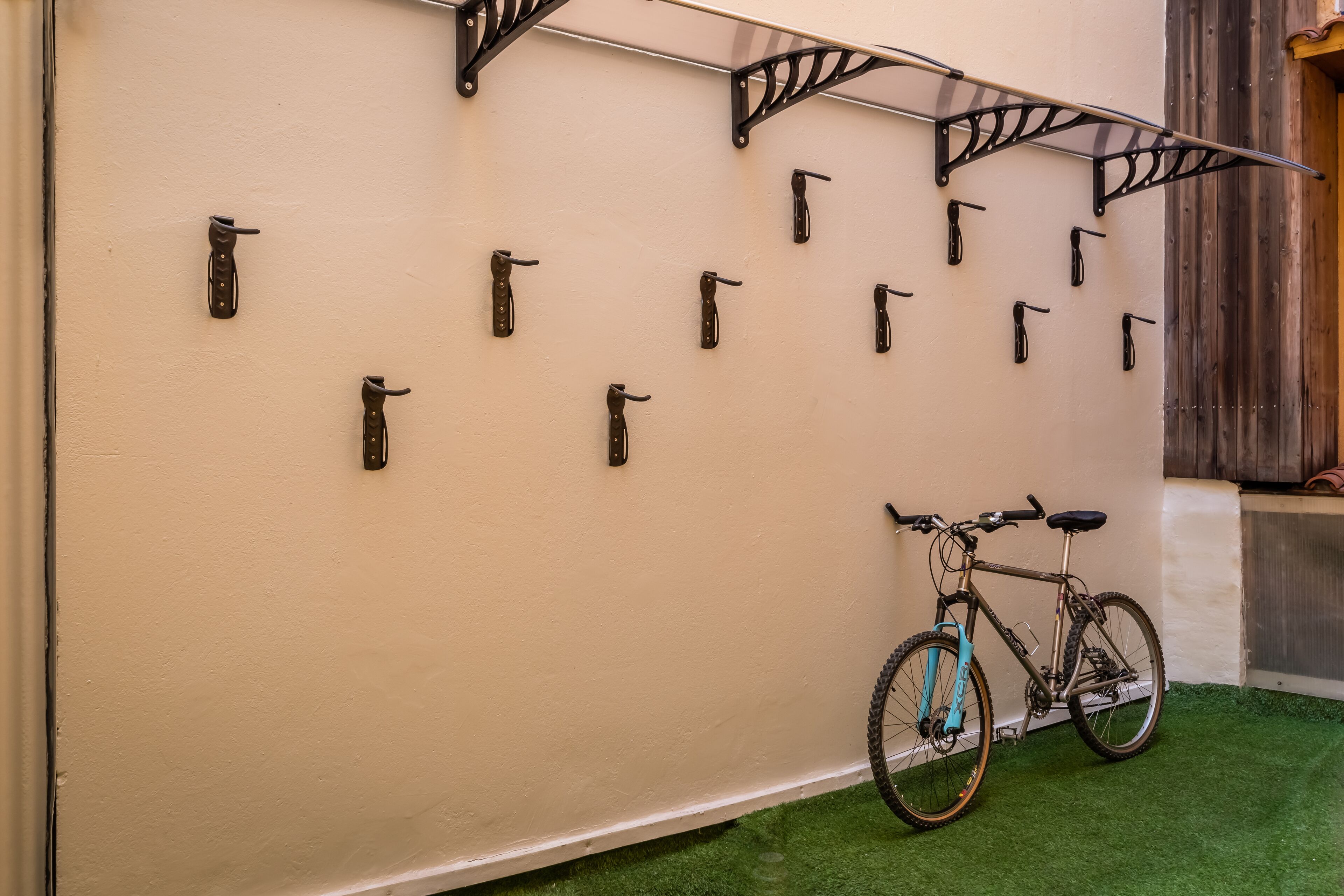 A wall with multiple hooks for hanging items, a bicycle leaning against it, and a green artificial turf floor.
