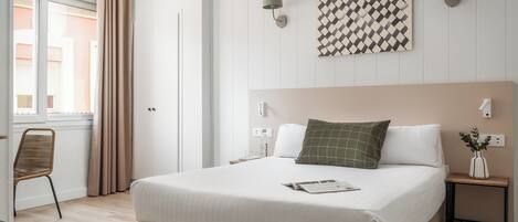 A neatly arranged bedroom with a large bed, bedside tables, a chair, and a window with curtains.