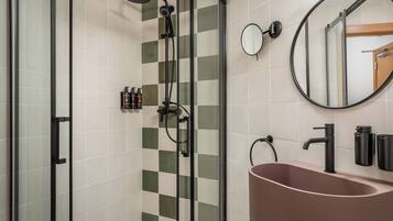 Een moderne badkamer met een douchecabine van glas, een ronde spiegel, een roze wastafel en een toilet.