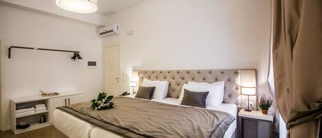 A modern hotel room with a large bed, bedside lamps, a bedside table with a plant, and a headboard with a tufted design.