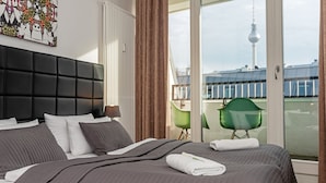 A modern hotel room with a large bed, a view of a tower, and a green chair by the window. - Apartments Rosenthal Residence (Berlin)