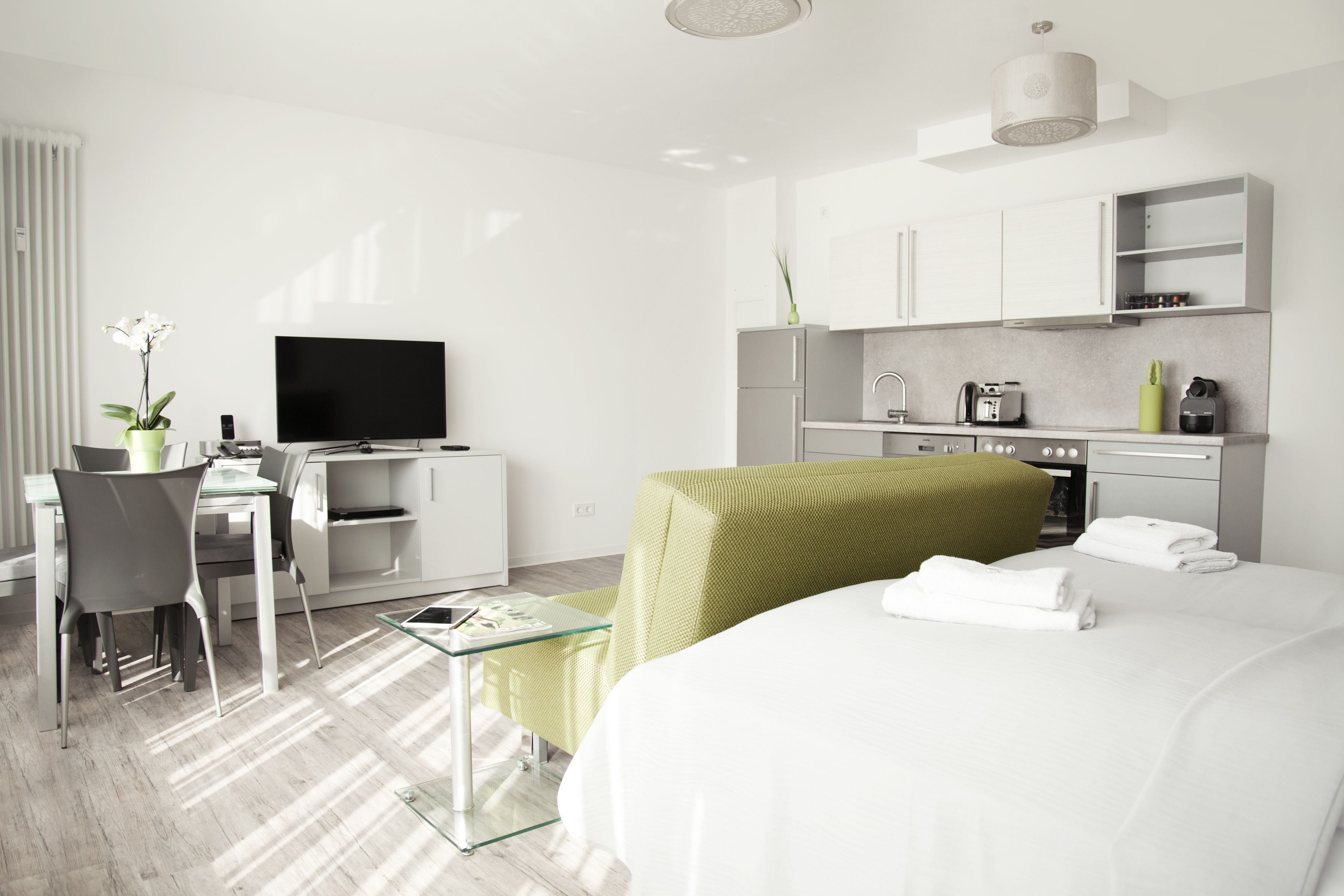 Ein modernes Hotelzimmer mit einem Bett, einem Schreibtisch mit Computer, einem Fernseher und einer Küchenzeile.