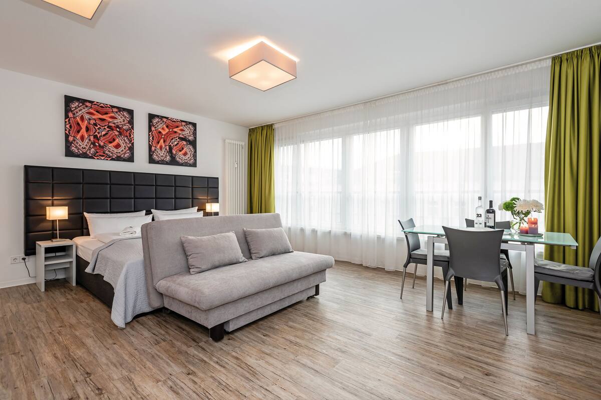 Moderni hotellihuone, jossa on sänky, sohva, ruokapöytä, tuolit ja taideteoksia seinillä.