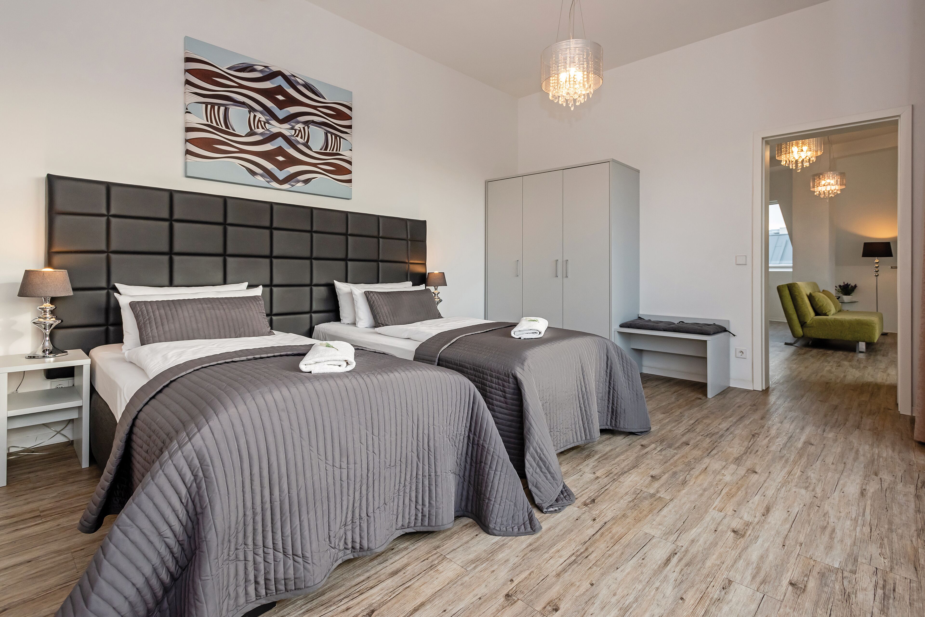 A modern bedroom with two beds, a large wardrobe, and a chandelier.