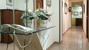 Zona de recepción de hotel con un mostrador de cristal, un teléfono y arreglos florales.