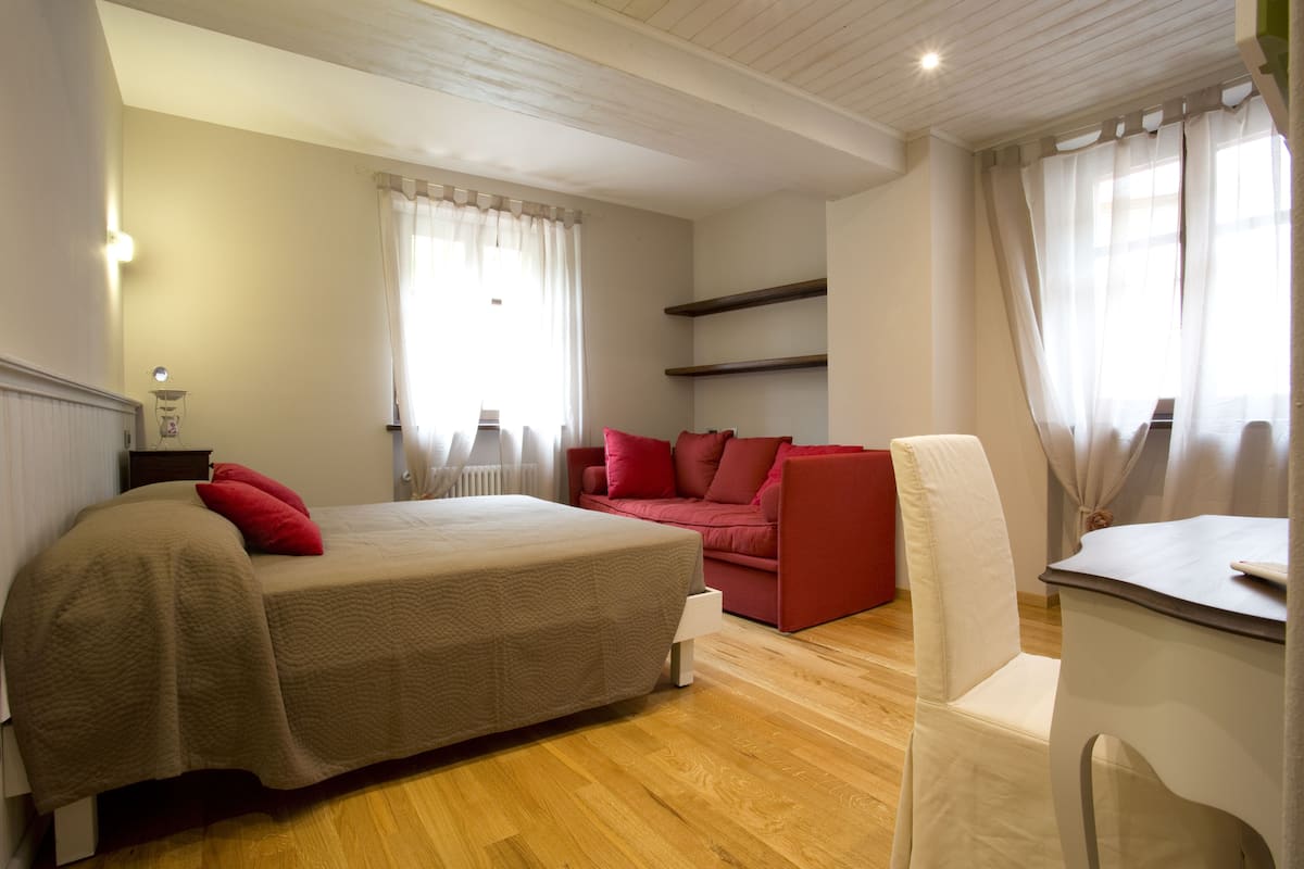 Ein Schlafzimmer mit einem Bett, einem roten Sofa, einem weißen Sessel und einem kleinen Tisch.
