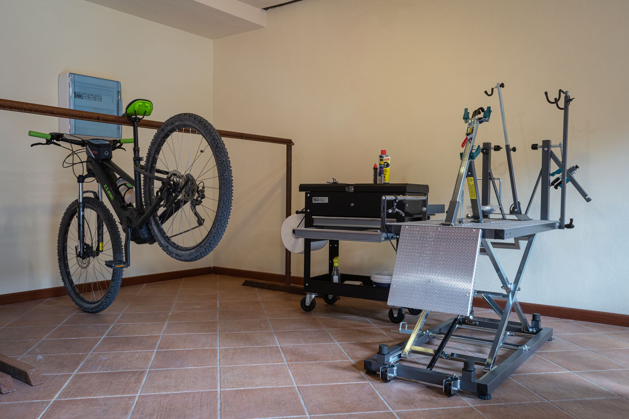 Una habitación con una bicicleta colgada en la pared, un banco de trabajo con herramientas y una estructura de metal.