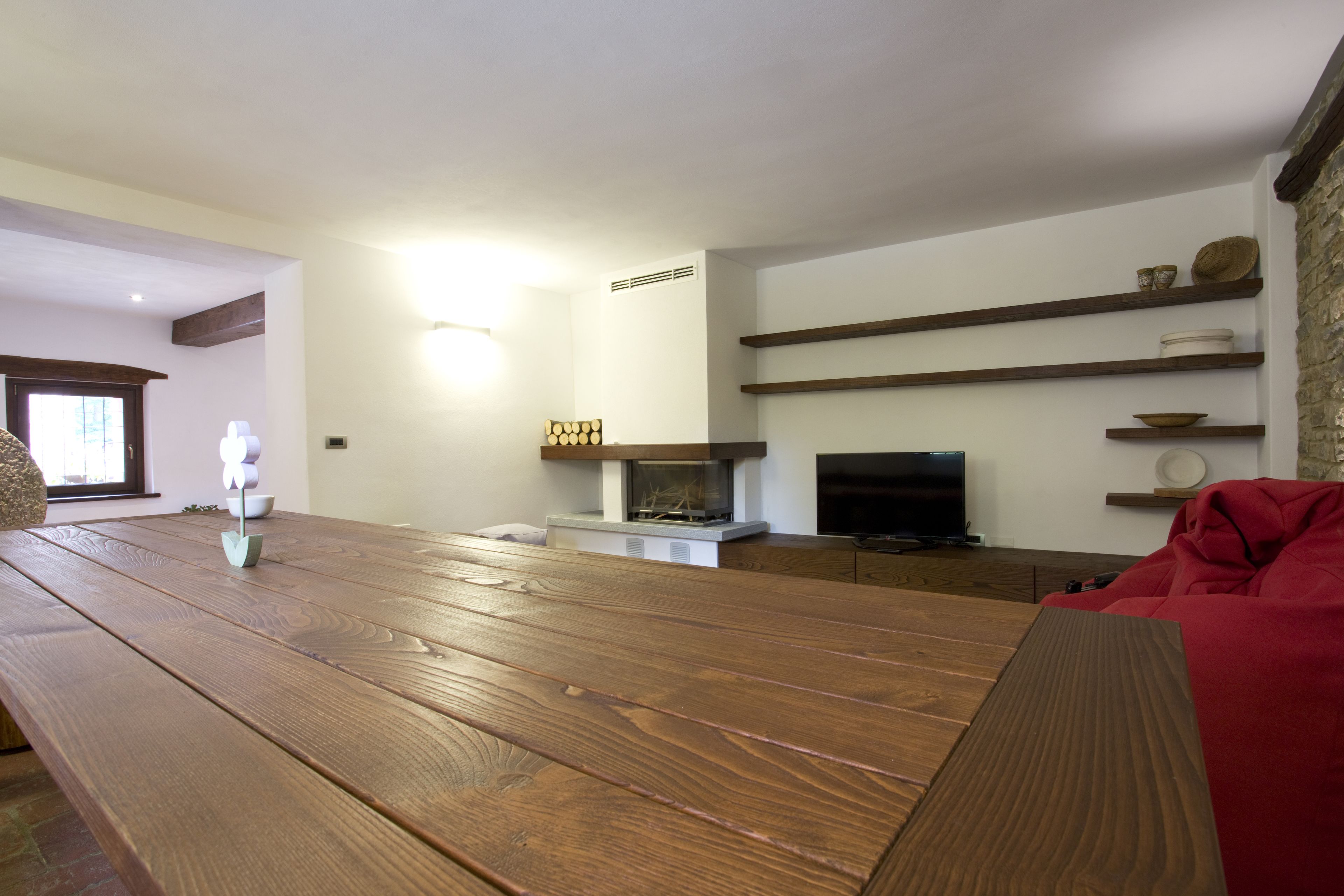 A living room with a wooden table, a fireplace, shelves with decorative items, and a red sofa.