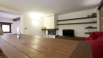 A living room with a wooden table, a fireplace, shelves with decorative items, and a red sofa.
