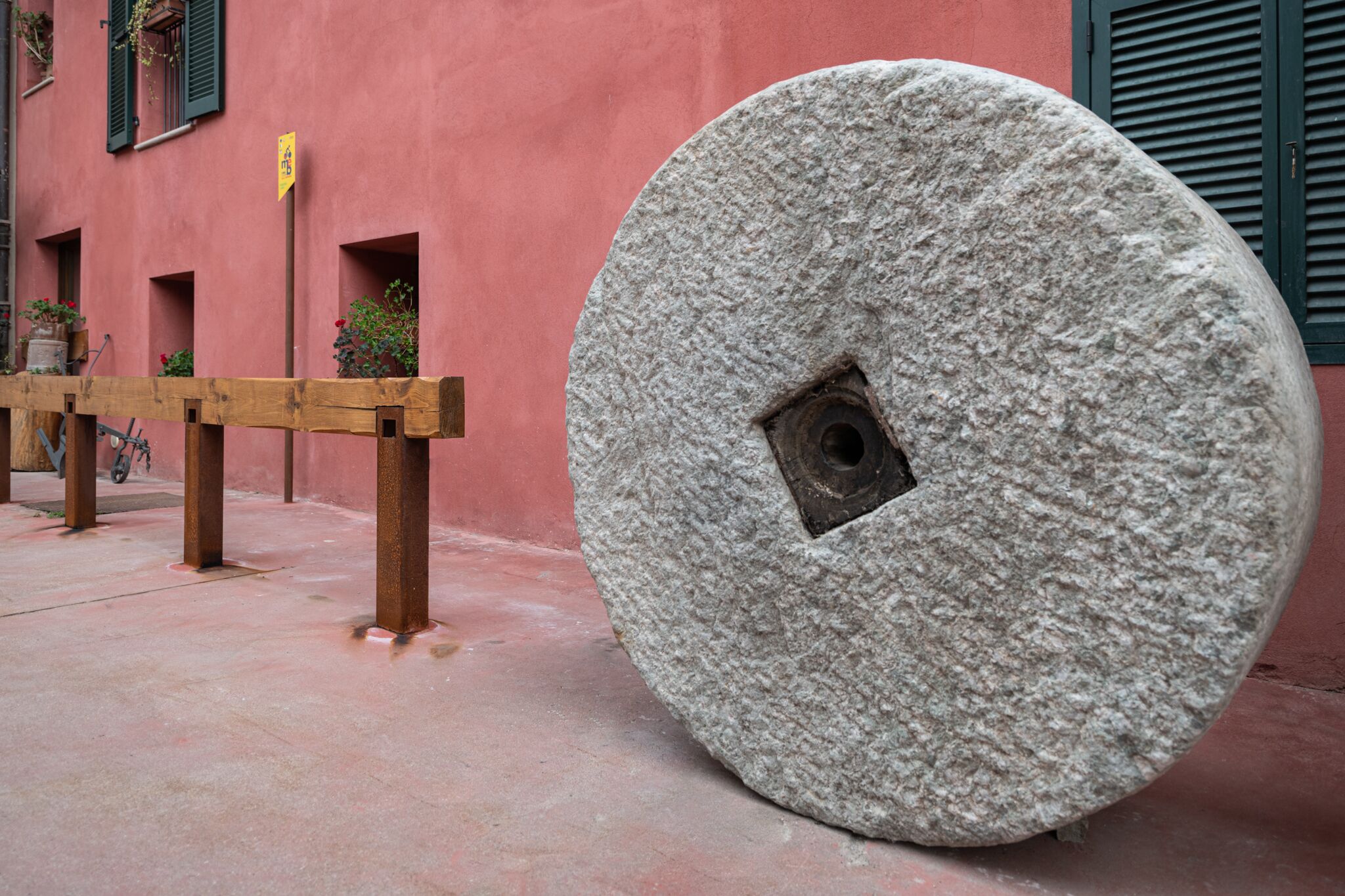 Una gran rueda de piedra frente a un edificio rosa con contraventanas verdes.