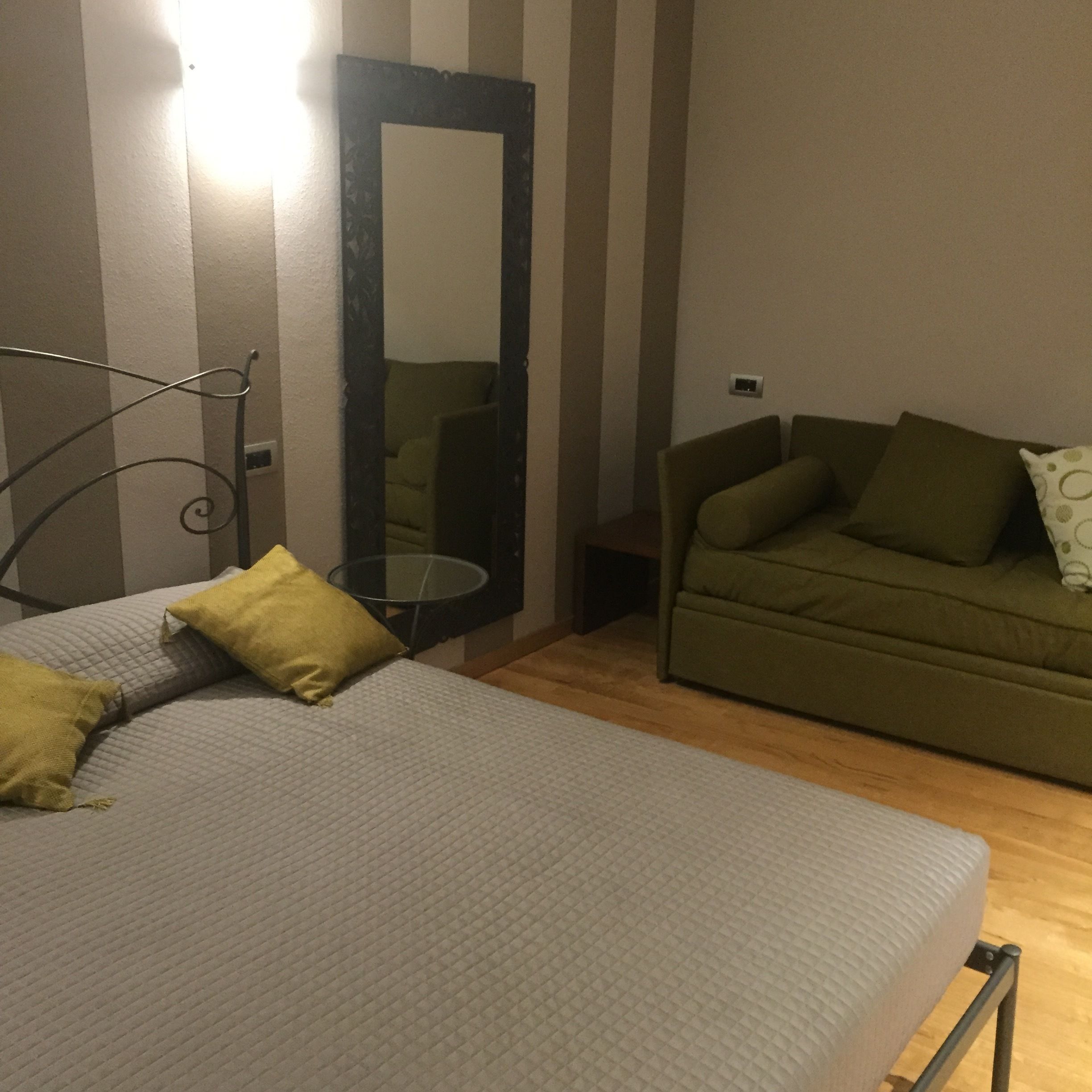 A room with a bed, a green sofa, a small table, and a mirror.