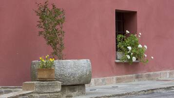 A stone planter with yellow flowers and a potted plant with white flowers against a red wall.