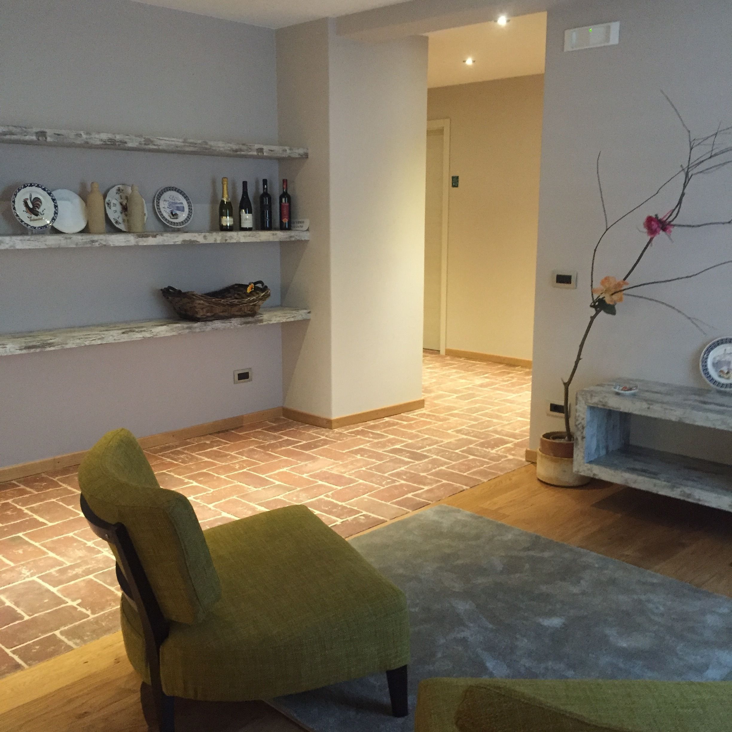 A living room with a green armchair, a shelf with wine bottles, and a potted plant.