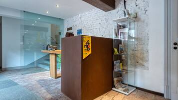 Een receptiegedeelte met een houten balie, een glazen displaykast met tijdschriften en een witte bakstenen muur.