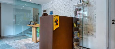 Ein Empfangsbereich mit einem Holztisch, einer Glastheke mit Zeitschriften und einer Wand aus weißen Ziegeln.
