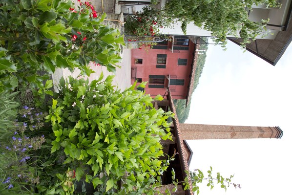 Un edificio de fachada roja, con una chimenea visible y un balcón adornado con flores rojas.
