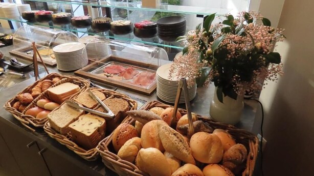 A buffet with various breads, pastries, and a floral arrangement. - Adagio hotel (Knokke-Heist)
