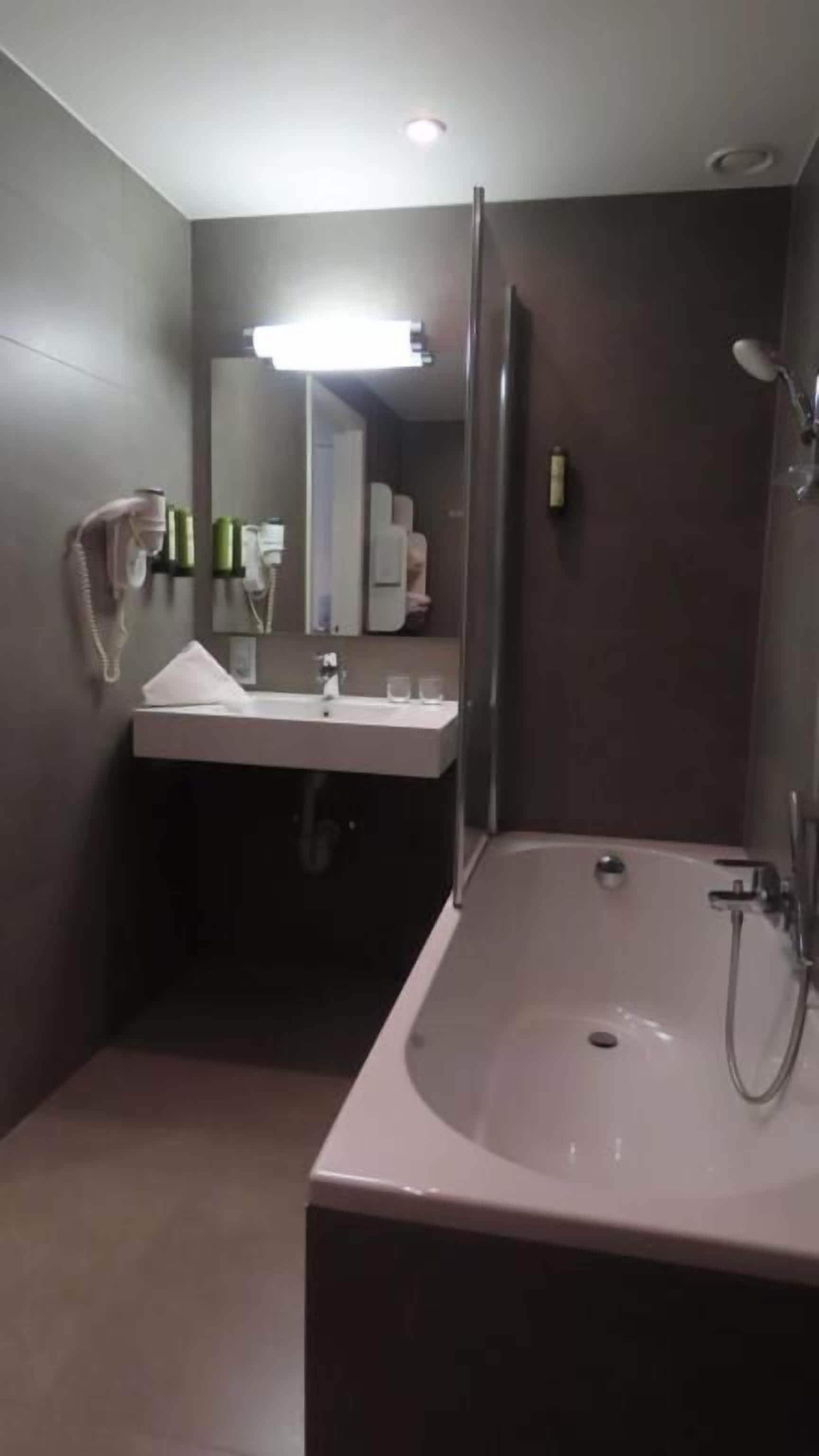 Une salle de bain moderne avec une grande baignoire, un lavabo avec un miroir et un sèche-cheveux fixé au mur.
